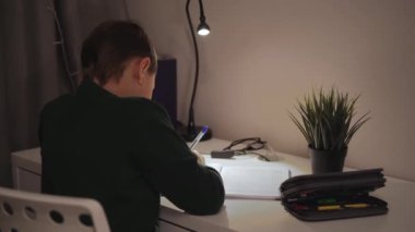 Karanlık odada ışığın altında ödev yapan bir çocuğun arka görüntüsü. Yüksek kaliteli FullHD görüntüler