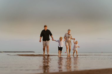 Kafkasyalı güzel bir aile gün batımında denizde koşuyor. Çocuklarla yaz tatili. Yüksek kalite fotoğraf