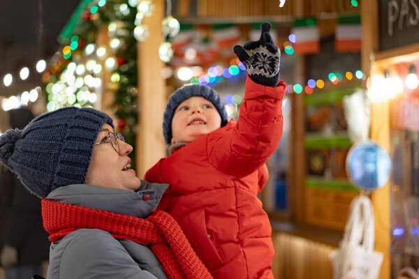 cute baby girl on mother hands outdoors at christmas market. Image with selective focus and noise effect