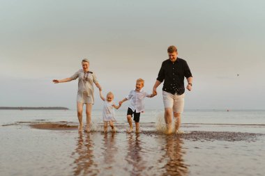 Kafkasyalı güzel bir aile gün batımında denizde koşuyor. Çocuklarla yaz tatili. Yüksek kalite fotoğraf