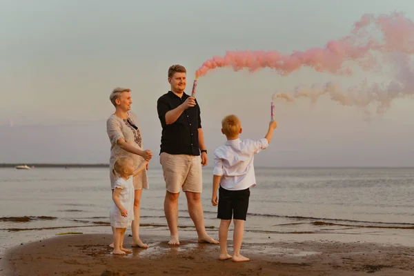 Gender reveal announcement with pink smoke on beach. Family expecting baby girl. High quality photo