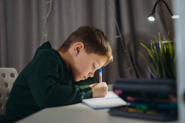 Kafkasyalı çocuk karanlık odada lambanın ışığında ödev yapıyor. Seçici odaklı resim