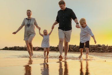 Kafkasyalı güzel bir aile gün batımında denizde koşuyor. Çocuklarla yaz tatili. Yüksek kalite fotoğraf