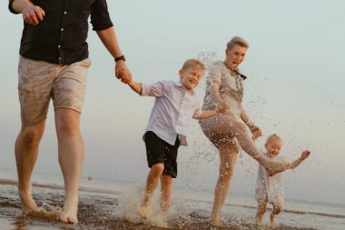 Kafkasyalı güzel bir aile gün batımında denizde koşuyor. Çocuklarla yaz tatili. Yüksek kalite fotoğraf