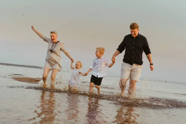Kafkasyalı güzel bir aile gün batımında denizde koşuyor. Çocuklarla yaz tatili. Yüksek kalite fotoğraf