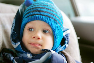Çocuk emniyet koltuğunda oturan sevimli bir çocuk. Üzerinde kışlık tulum ve şapka var. Seçici odaklı resim