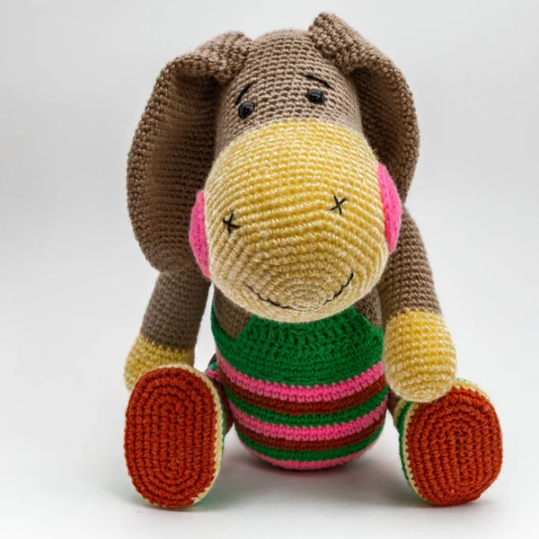 Amigurumi eşeği çok renkli giysiler içinde oturur. İzole et.