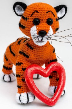 El yapımı amigurumi bebek kaplan yavrusu kırmızı bir kalbin yanında duruyor.