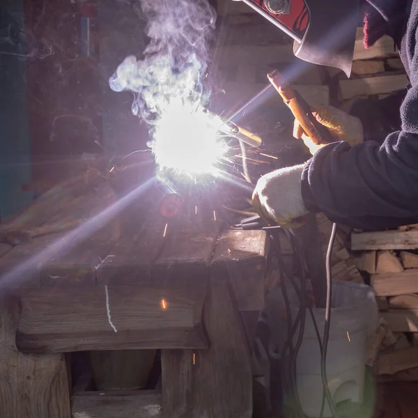 Koruyucu maskeli bir adam metal bir çubuğu elektrot ile kaynaştırıyor..