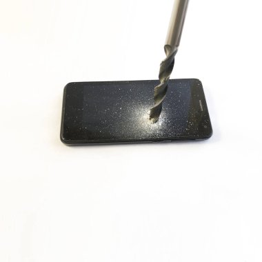 Metal bir matkap siyah bir akıllı telefonun ekranını deliyor.