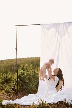 Tarlada beyaz bir bez üzerinde bebekle güzel bir annenin portresi.