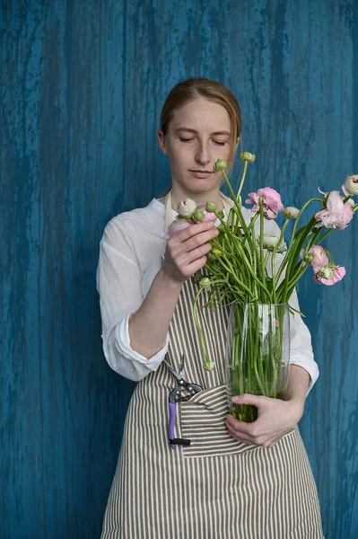 Mavi arka planda elinde buketle genç ve güzel bir çiçekçinin portresi.