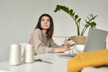 Genç, güzel bir terzi evde kıyafet yapıyor. Masada duran ve dizüstü bilgisayarla çalışan bir kadın.