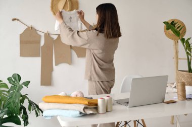 Genç ve güzel bir tasarımcı kıyafetlerini elinde tutuyor ve kalitesine bakıyor.