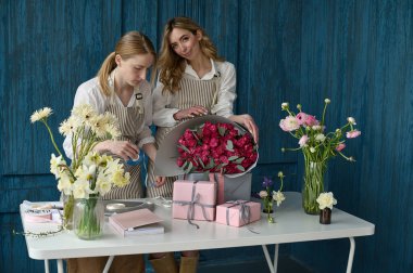 Takım çalışması. İki güzel çiçekçi mavi arka planda bir buket oluşturuyor.