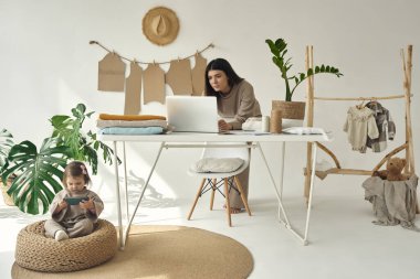 Genç, güzel bir terzi evde kıyafet yapıyor. Masada duran ve dizüstü bilgisayarla çalışan bir kadın.
