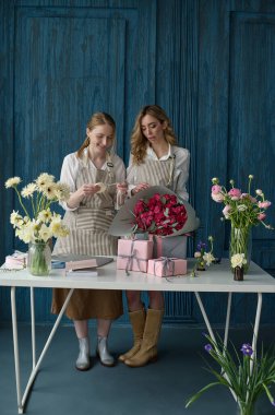 Takım çalışması. İki güzel çiçekçi mavi arka planda bir buket oluşturuyor.