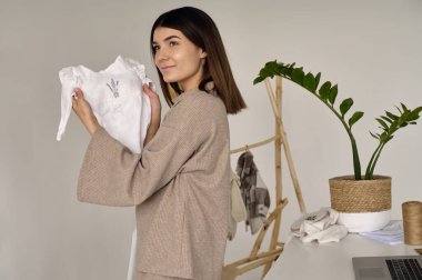 Genç ve güzel bir tasarımcı kıyafetlerini elinde tutuyor ve kalitesine bakıyor.