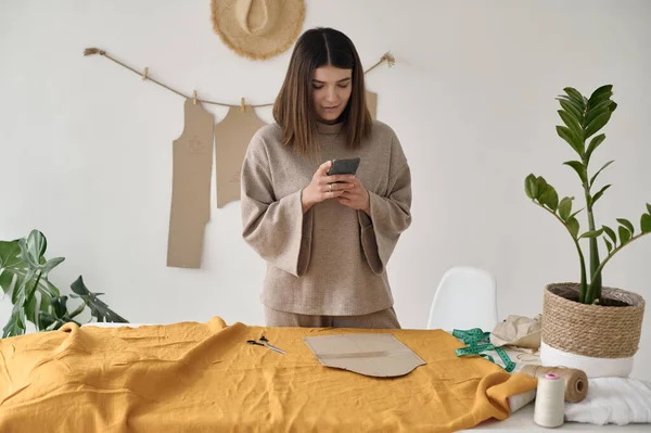 Genç, çekici bir tasarımcı masanın önünde çalışıyor. Üzerinde kumaş ve desen var.