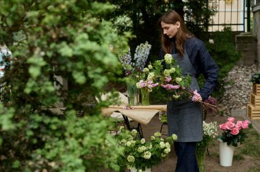 Güzel, genç bir çiçekçi yeşil terasta buket yapıyor.