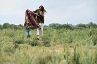 Genç ve güzel anne doğada küçük kızıyla oynuyor.