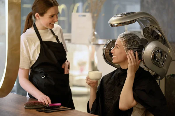 young woman under hooded dryer machine in hair salon