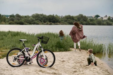Genç anne bisikletlerin yanında iki çocuğuyla oynuyor.