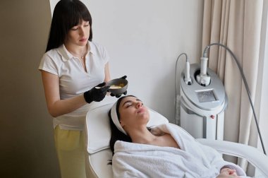 Yüz soyma maskesi, kaplıca güzellik tedavisi, cilt bakımı. Güzellik salonunda güzellik uzmanı bir kadının yüz bakımını alıyor.