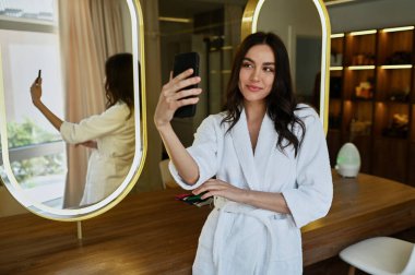 Beyaz önlüklü bir güzellik salonundaki genç güzel kız selfie çekiyor. Gelinin sabah konsepti