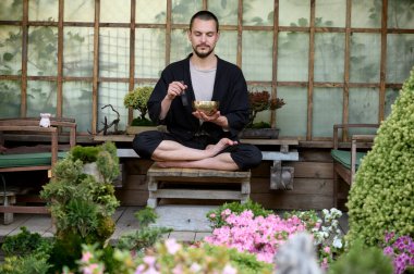 Genç yakışıklı bir adam, kazançlı bir çardakta şarkı söyleyen bir kaseyle meditasyon yapıyor.