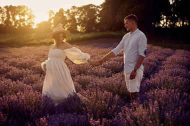 Gün batımında lavanta tarlasında yürüyen genç ve güzel hamile bir çift. Mutlu aile kavramı