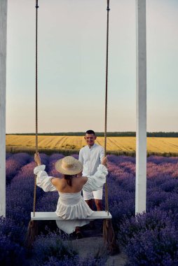 young beautiful pregnant couple on a swing in a lavender field at sunset