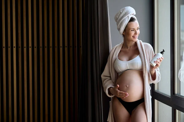 Retrato Uma Bela Mulher Grávida Roupão Toalha Aplica Creme Barriga — Fotografia de Stock