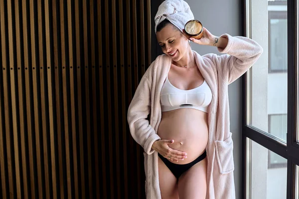 Όμορφη Έγκυος Γυναίκα Μπουρνούζι Απλώνει Μια Κρέμα Στην Κοιλιά Της — Φωτογραφία Αρχείου