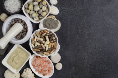 Kapsüllerdeki besin takviyeleri, tabaklarda ve havanda tuz ve deniz minerallerinden oluşan çeşitli kristaller. Beyaz, gri, pembe tuz, deniz kabukları ve siyah zemin üzerinde deniz çakıl taşları. 