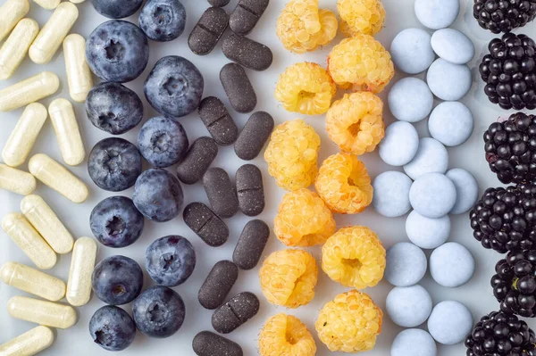 Свежие ягоды, таблетки и капсулы на белом фоне — стоковое фото