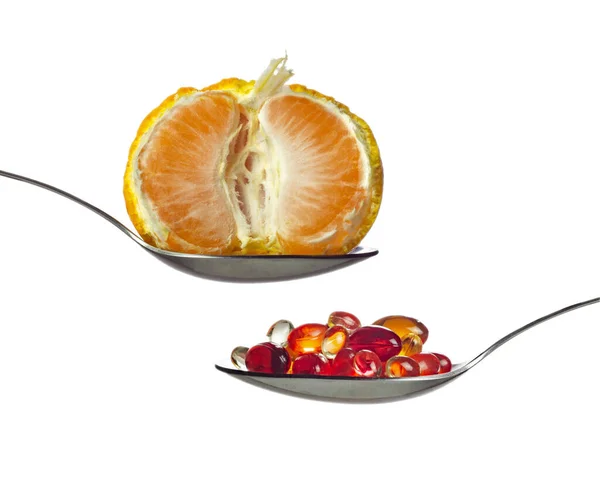 Vitaminli kırmızı şeffaf kapsüller ve yarım kaşık mandalina. — Stok fotoğraf