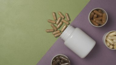 Yeşil ve mor arka planda beyaz plastik kavanozlarda besin takviyeleri bulunan çeşitli kapsüller