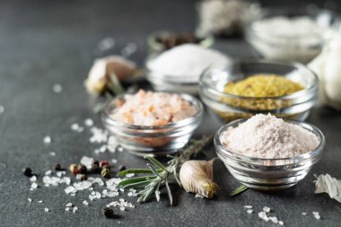 Different types of salt and culinary spices in glass plates on a dark background