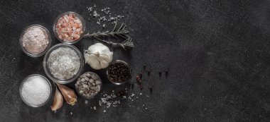 Different types of salt and culinary spices in glass plates on a dark background
