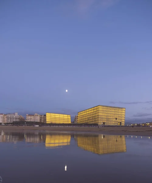 full moon over the zurriola beach. The buildings of the city are reflected in the sea water, Donostia-San Sebastian, Basque Country.