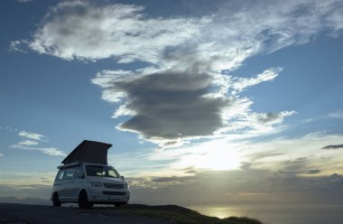 Gün batımında okyanusun önünde, dağda duran kampçı. 