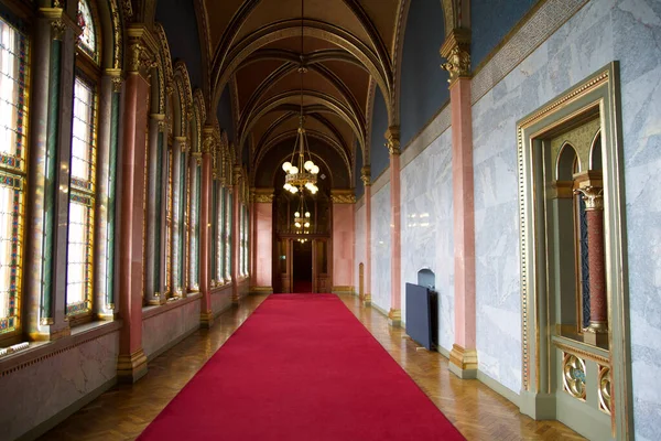 БУДАПЕСТ, ХАНГАРИЯ - 03 МАР 2019: Длинный коридор с красной ковровой дорожкой на мраморном полу и люстрой на потолке в здании парламента Венгрии — стоковое фото