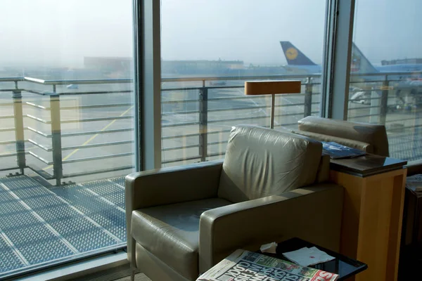 FRANKFURT, GERMANY - 11 NOV 2017: Comfortable lounge chair upholstered in light brown leather in the airport frequent flyer lounge with a view of the aircraft on the apron — стоковое фото