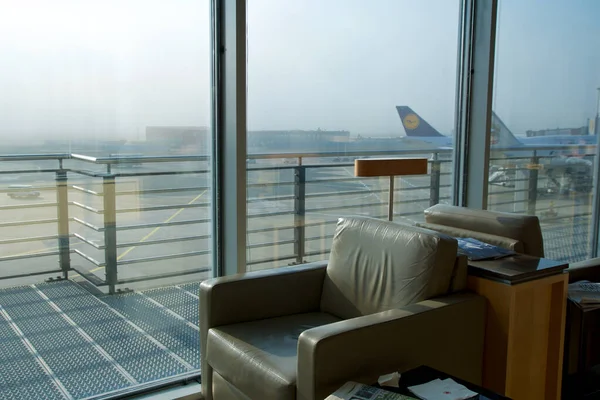 FRANKFURT, GERMANY - 11 NOV 2017: Comfortable lounge chair upholstered in light brown leather in the airport frequent flyer lounge with a view of the aircraft on the apron — стоковое фото