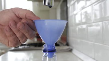 Bir Plastik Şişe Damlası 'nı bir huni kullanarak Taze Su ile doldurmak. Bir alıcıda su rezervi yapmak. Su Ekonomisi kavramı.