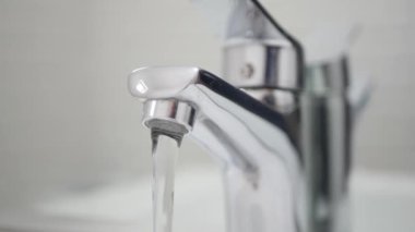 Ellerinde koruyucu eldivenler olan tıbbi kişi lavabo musluğunu banyodan kapatıyor..