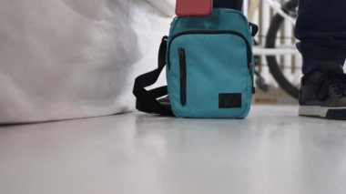 Cep telefonunu el çantasına koyup fermuarını kapatan bir adamla yakın çekim. Bir adam çantasını alıp odayı terk ediyor..