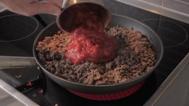 Chef pour in tomato sauce in minced meat in a frying pan. Frying minced meat in a pan, close-up.
