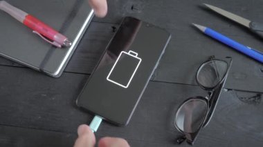 Charging a smartphone lying on a black wooden table. Connecting a USB cable to the phone. Electric charge.